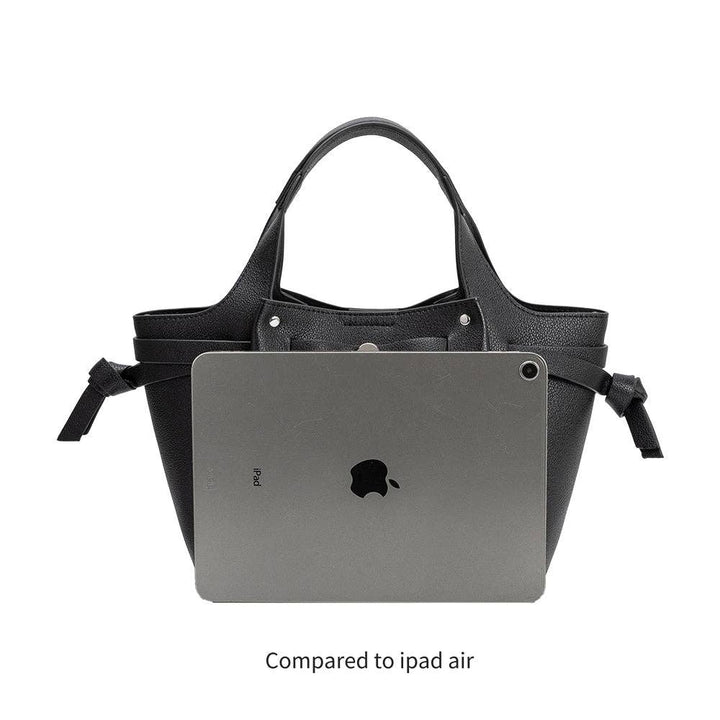 Black handbag with a laptop inside, compared to an iPad Air on a white background
