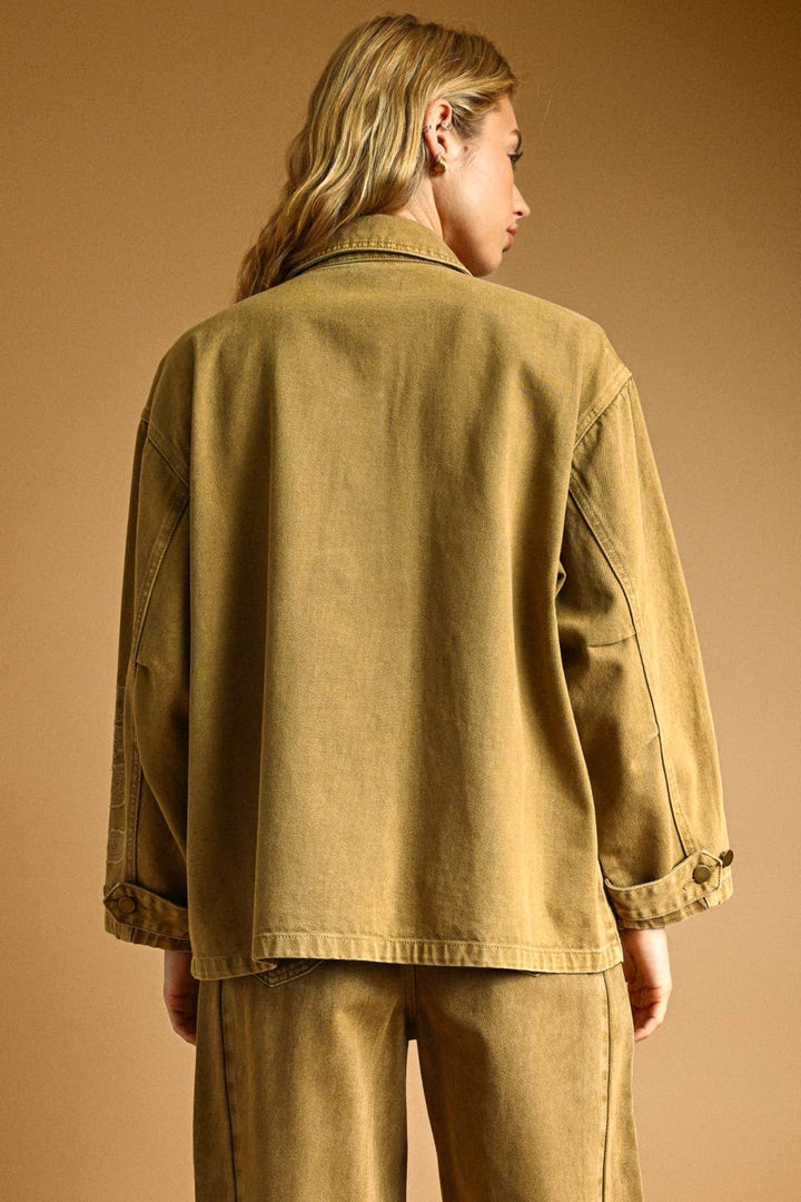 Woman wearing a beige denim jacket and pants matching set against a brown background