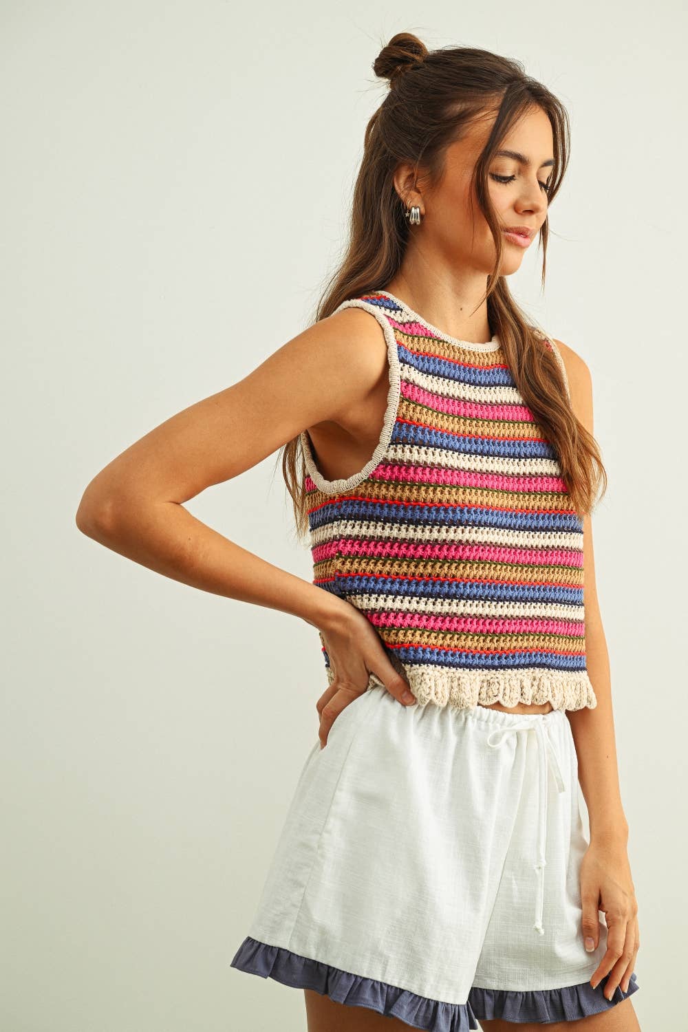 Woman wearing a colorful striped sleeveless crochet knit top and white shorts against a plain background