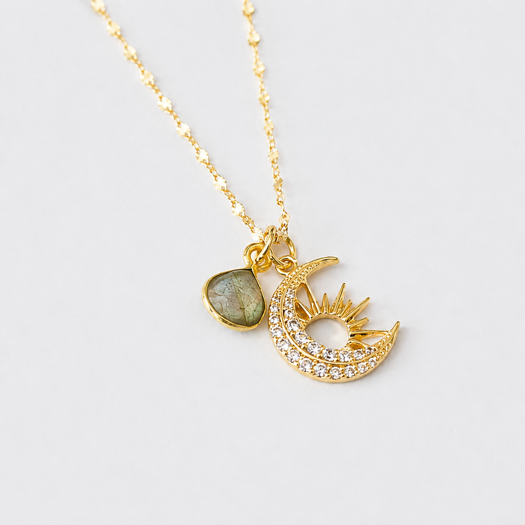 Gold necklace with moon and sun pendant and labradorite on a light gray background