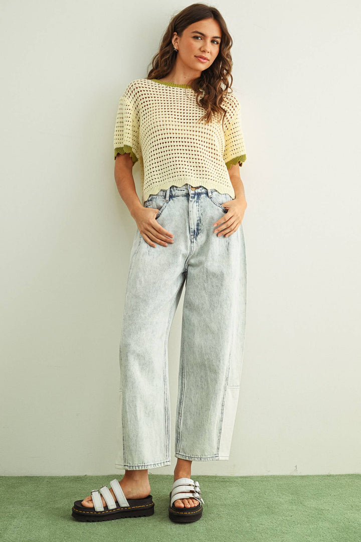 Woman wearing a white crochet knit top and light blue jeans against a plain background