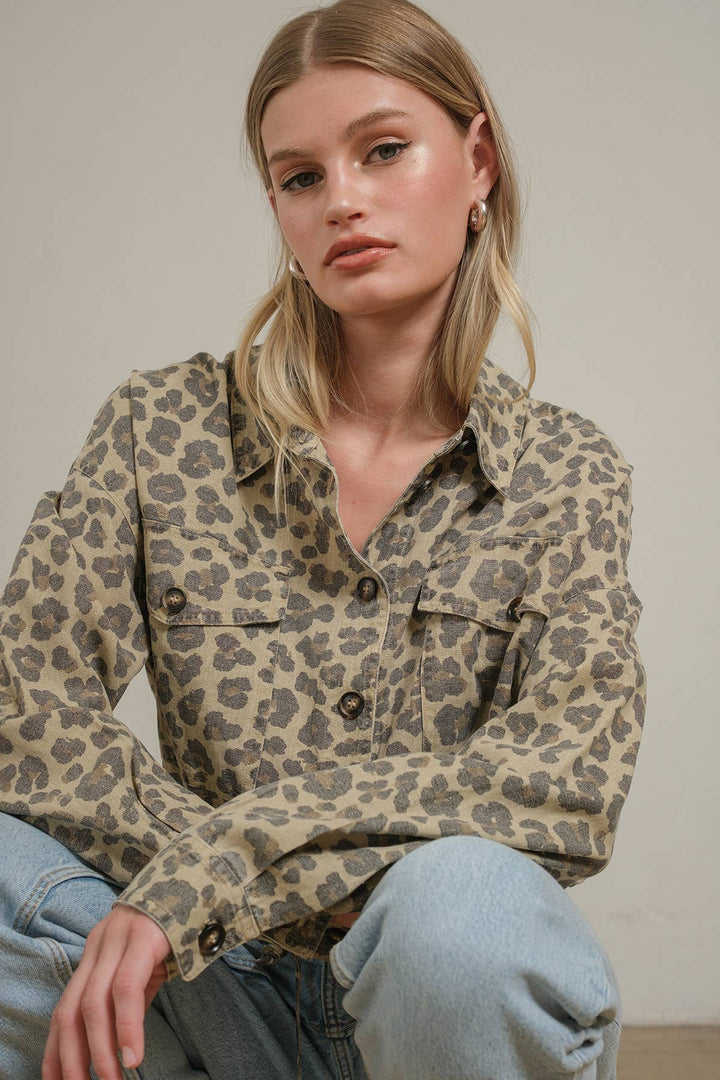 A woman wearing a beige and brown leopard-print button-up shirt with light blue jeans, posing against a neutral beige background.