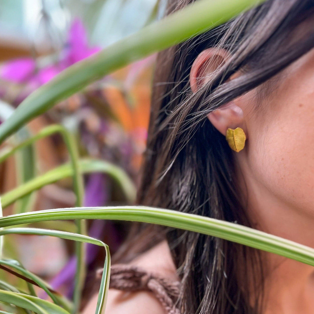 Close-up of a woman wearing a gold leaf shaped earring with plants in the background