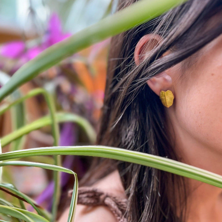 Close-up of a woman wearing a gold leaf shaped earring with plants in the background
