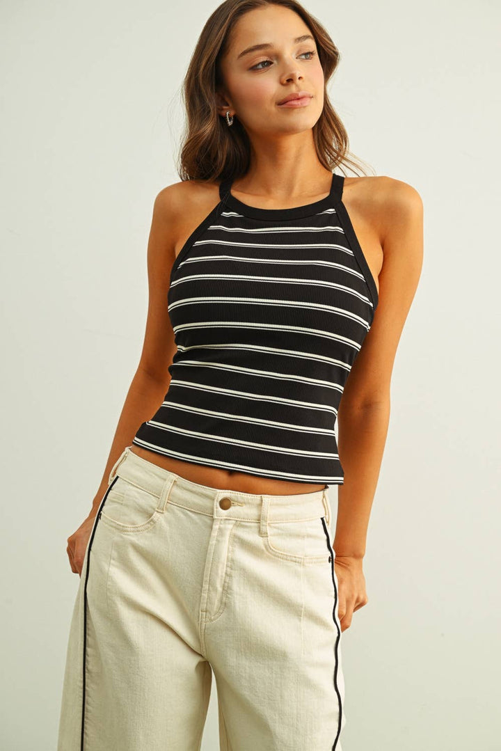 Woman wearing a black and white striped tank top with beige pants on a plain background