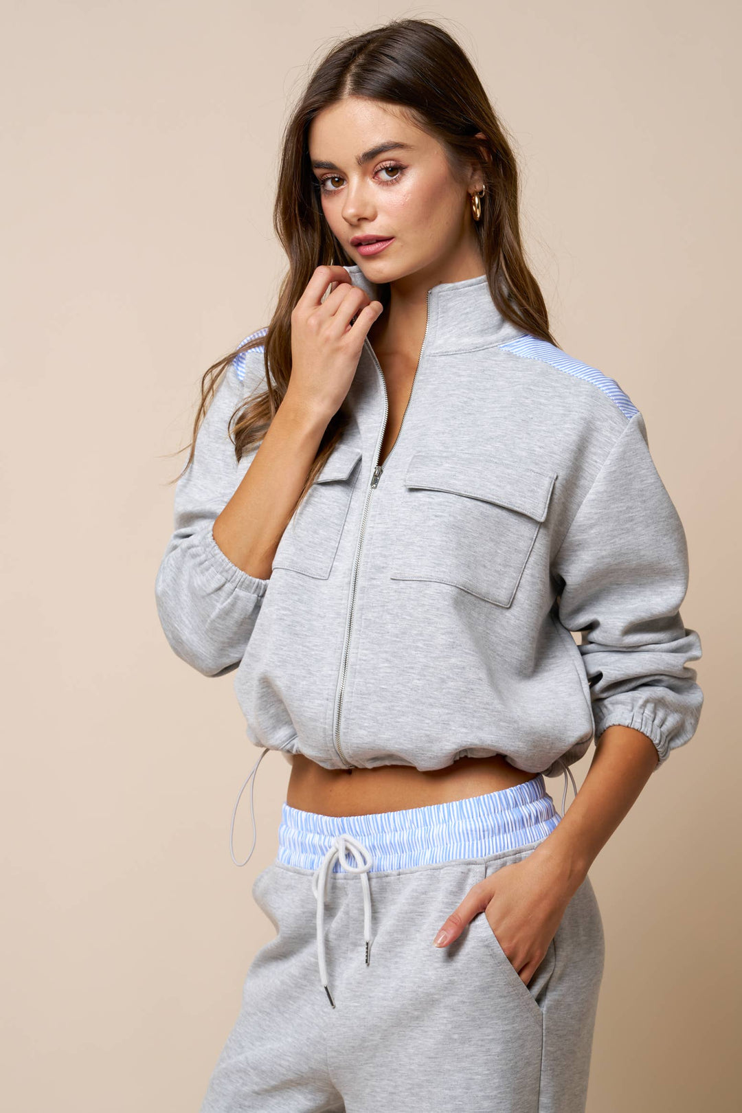 Woman wearing a gray bomber jacket with a beige background