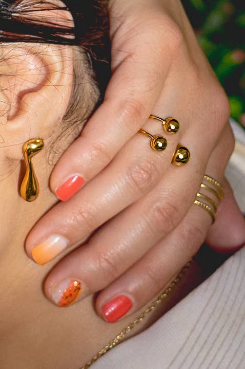 Close-up of a hand with gold rings and earrings.