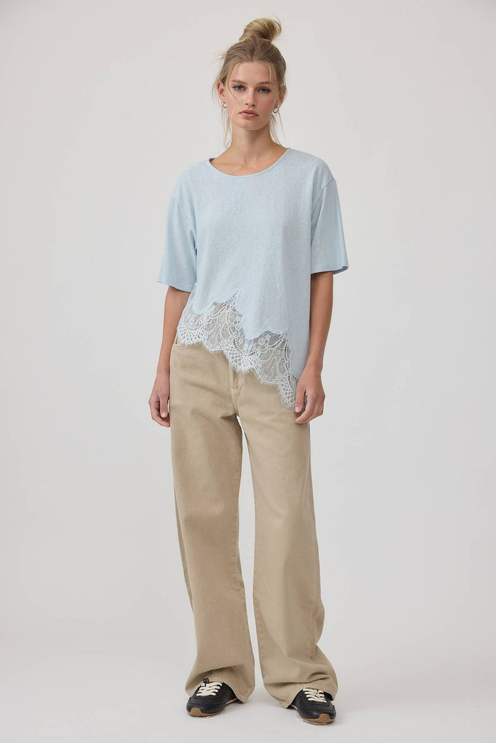Woman wearing a light blue top with lace detail and beige pants on a white background