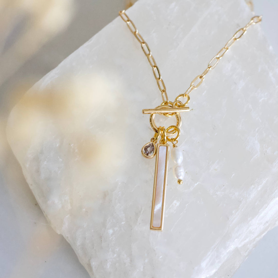 Gold charm necklace with mother of pearl pendant on a marble surface