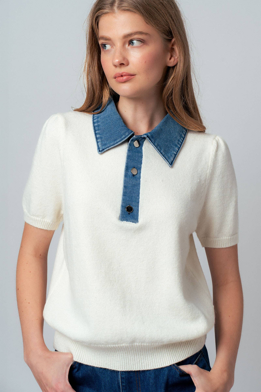 Woman wearing a white short sleeve sweater with a blue denim collar against a gray background