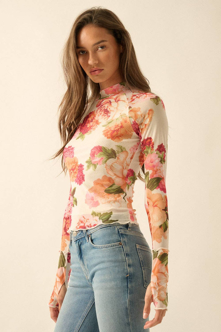Woman wearing a floral mesh long-sleeve top and jeans on a plain background