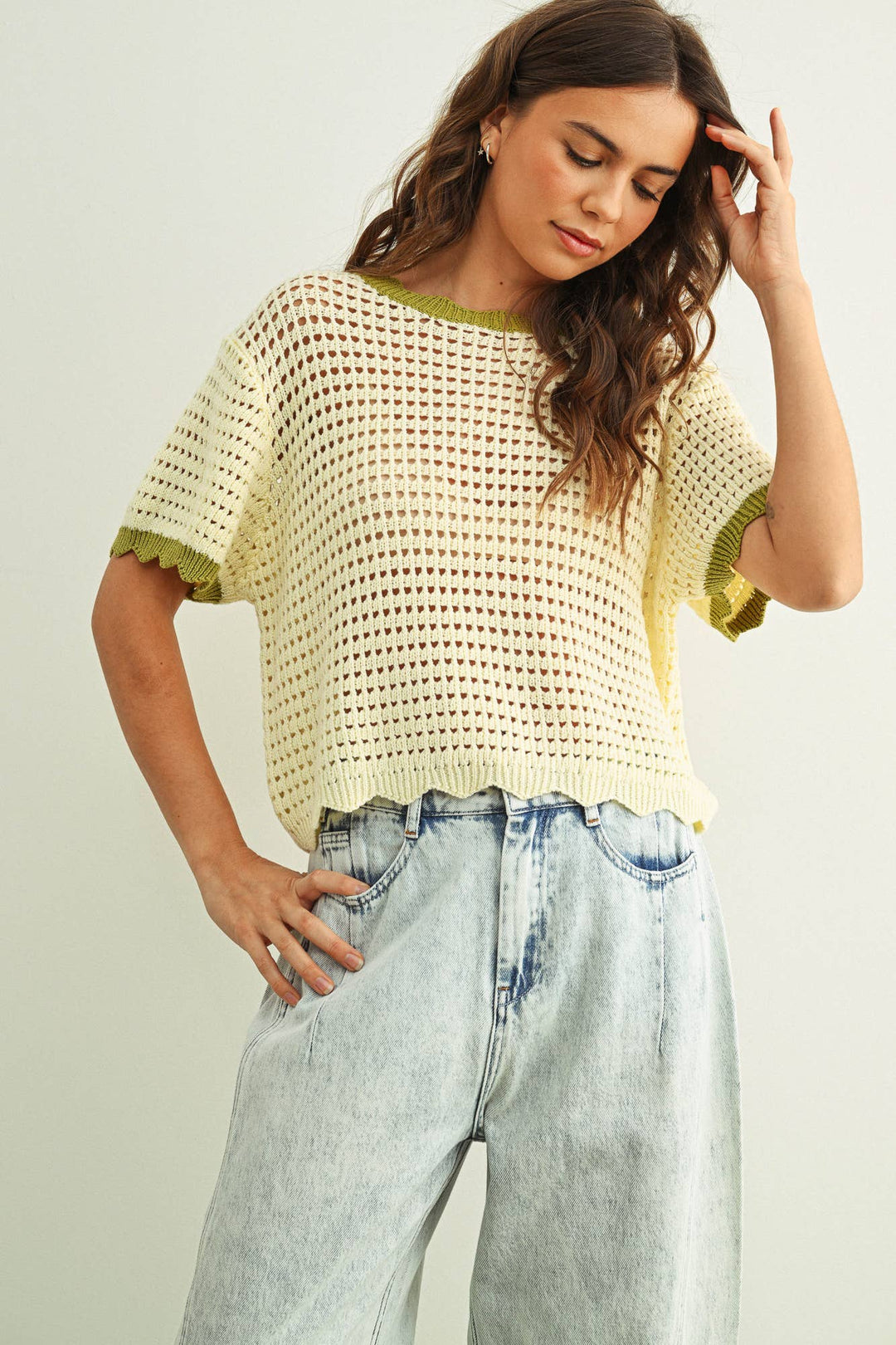 Woman wearing a white crochet top with scallop edge detail and light blue jeans against a plain background