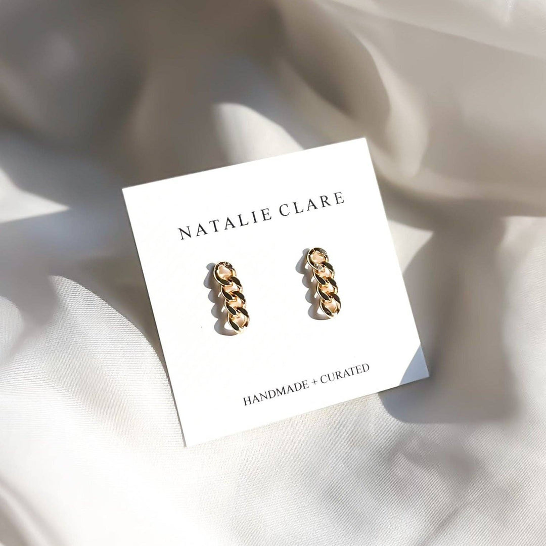Gold chain earrings on a 'Natalie Clare' branded card with a soft background