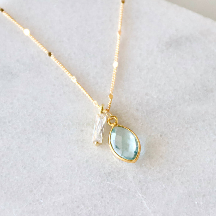 Gold necklace with a teardrop-shaped green gemstone pendant and cz charm on a white background