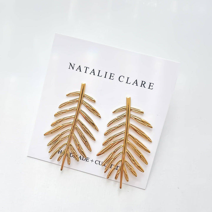 Gold leaf earrings on a white card with 'Natalie Clare' branding.