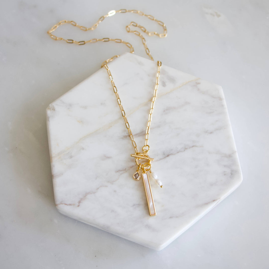 Gold necklace with a bar pendant with cz and pearl charms on a marble surface