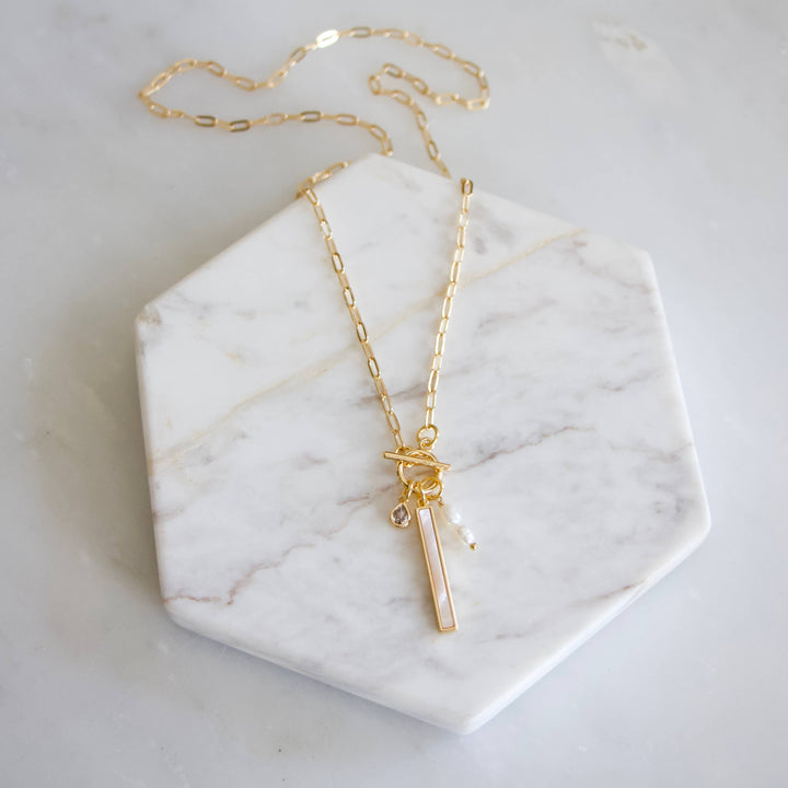 Gold necklace with a bar pendant with cz and pearl charms on a marble surface
