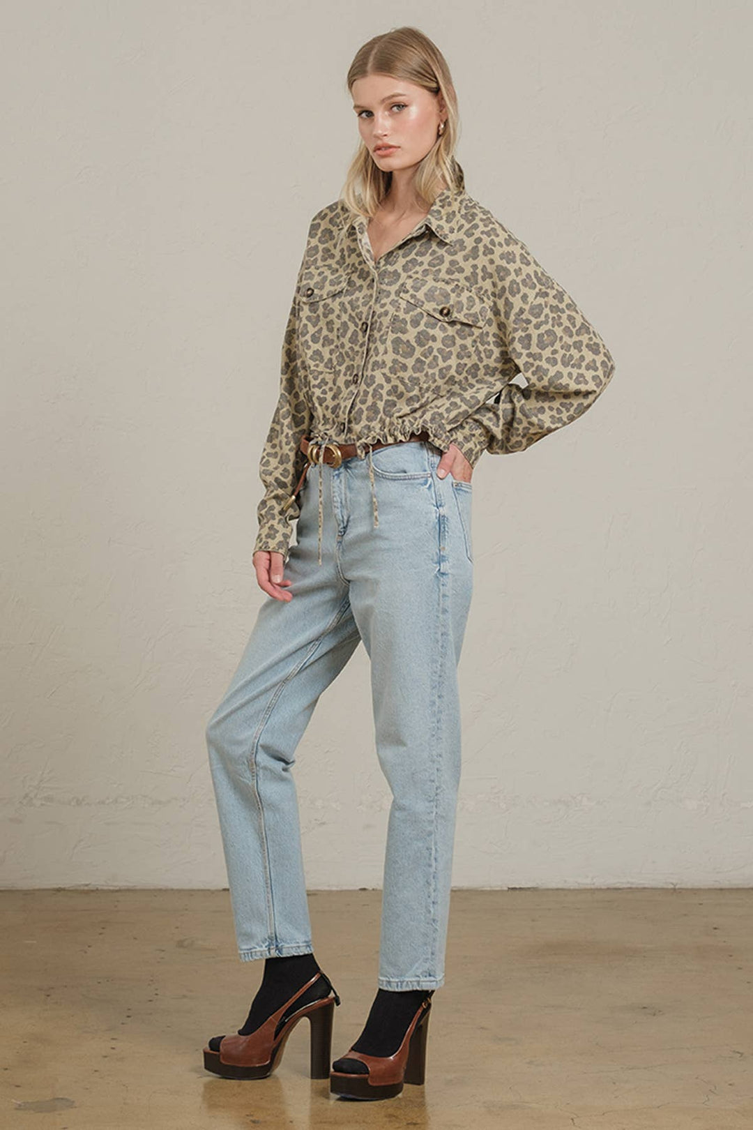 Woman wearing a leopard print shirt and light blue jeans against a plain background