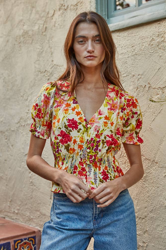 Woman wearing a colorful floral blouse and blue jeans against a textured wall.