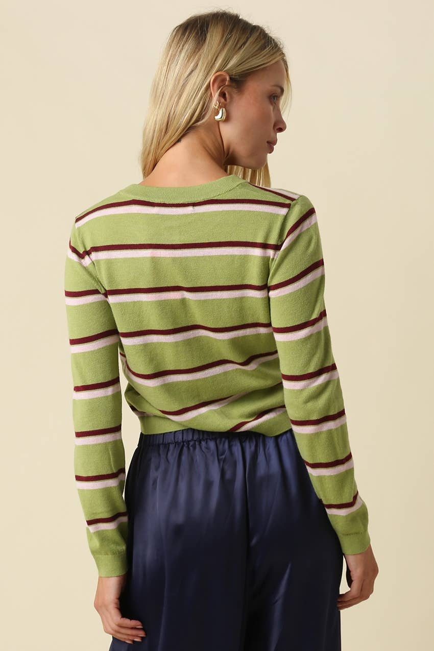 A woman shown from the back wearing a green long-sleeve knit top with horizontal burgundy and cream stripes, paired with dark navy pants, against a solid beige background.