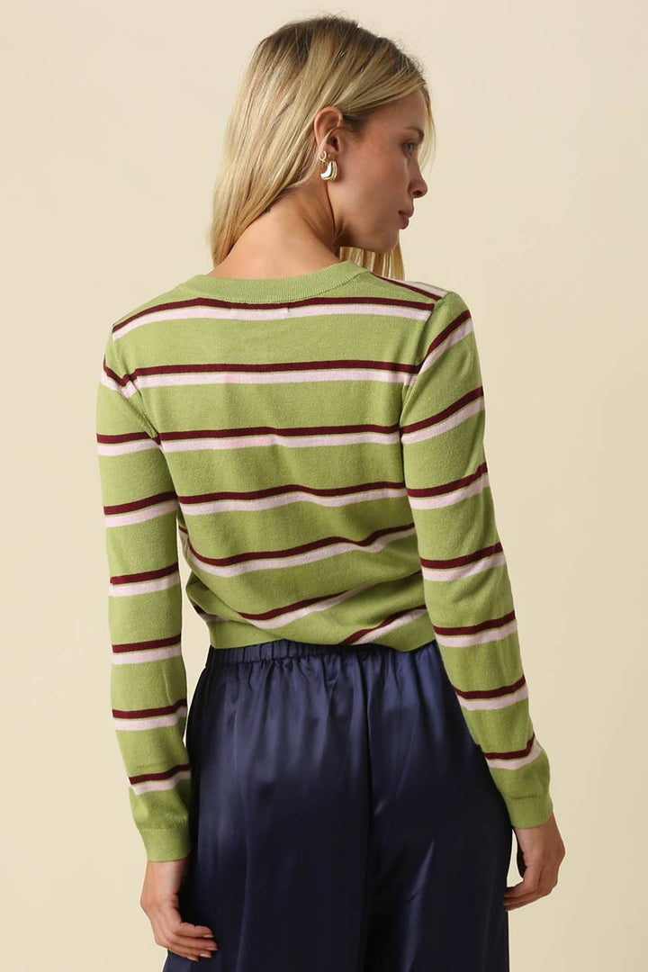 A woman shown from the back wearing a green long-sleeve knit top with horizontal burgundy and cream stripes, paired with dark navy pants, against a solid beige background.