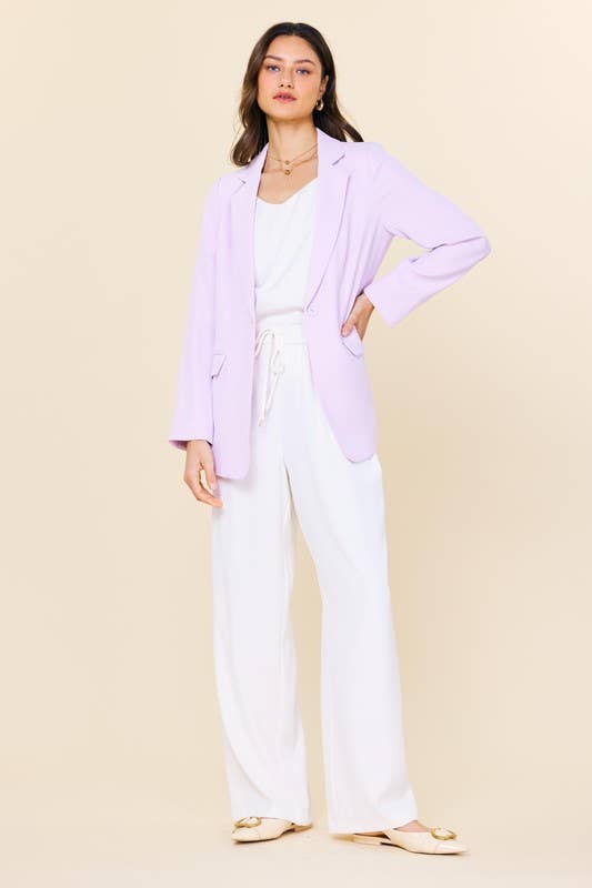 Woman wearing a light purple cardigan over a white top and pants on a beige background