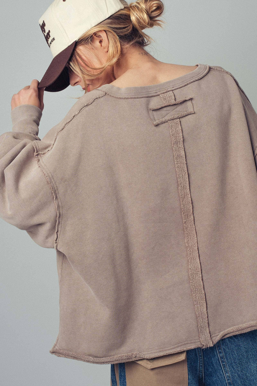 Person wearing a beige sweatshirt and blue jeans against a gray background