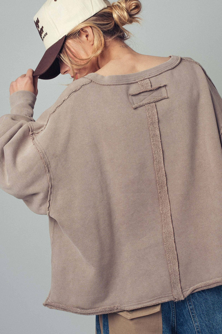 Person wearing a beige sweatshirt and blue jeans against a gray background