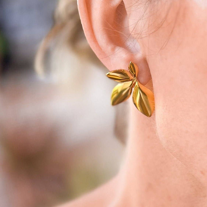 Gold leaf-shaped statement earring worn on an ear with a blurred background