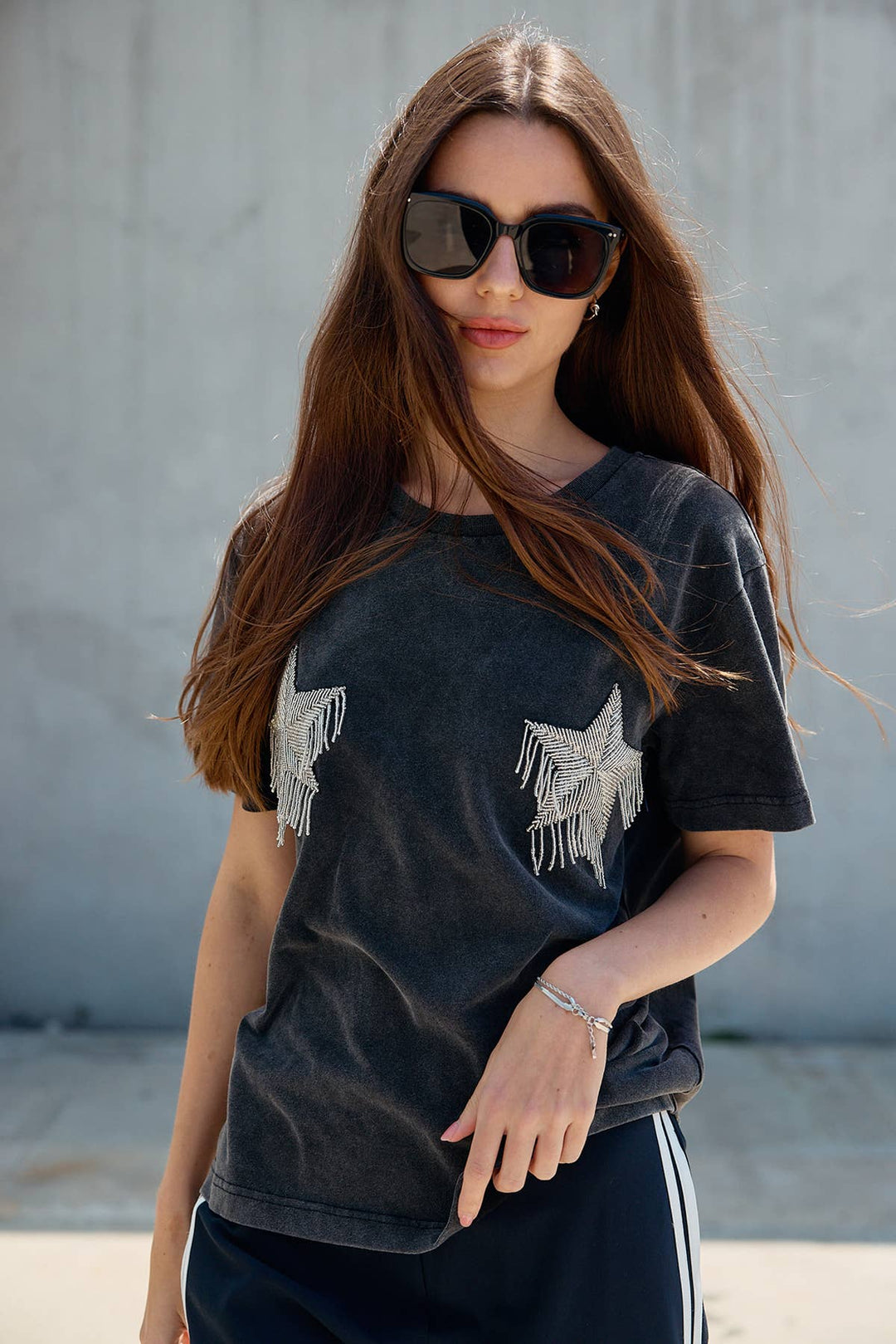 Woman wearing a black t-shirt with silver star designs and sunglasses against a gray background