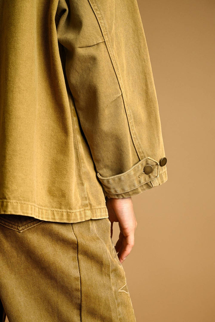 Close-up of a woman wearing a beige jacket and pants against a brown background