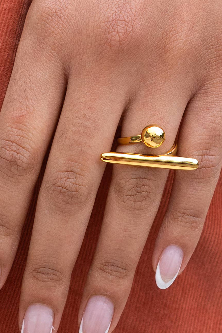 Gold ring with a spherical top on a hand against a red background