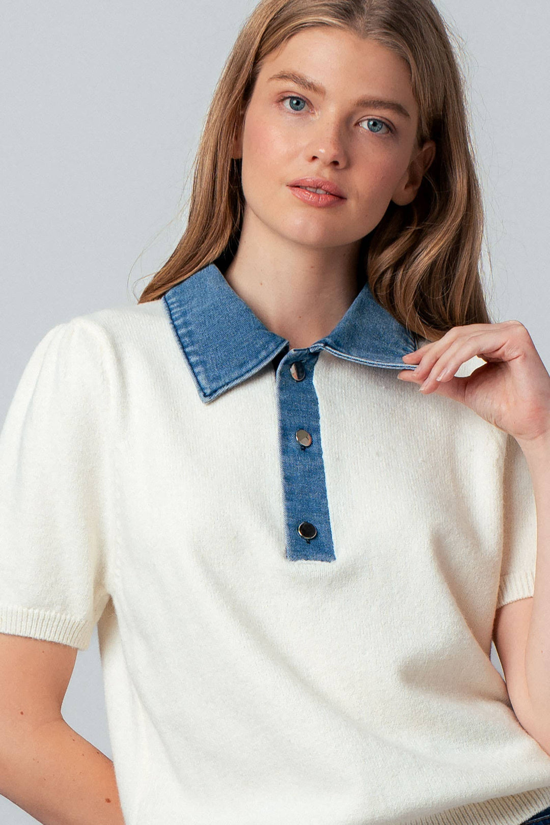 Woman wearing a white sweater with a blue denim collar against a plain background