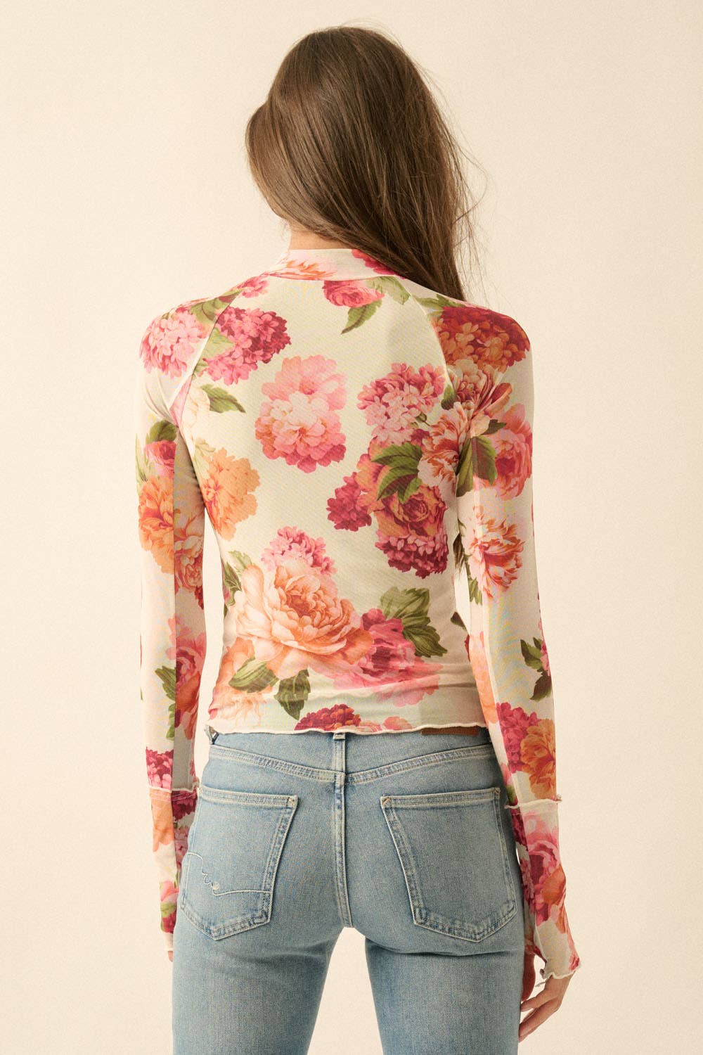 Woman wearing a floral mesh long-sleeve top and jeans on a plain background