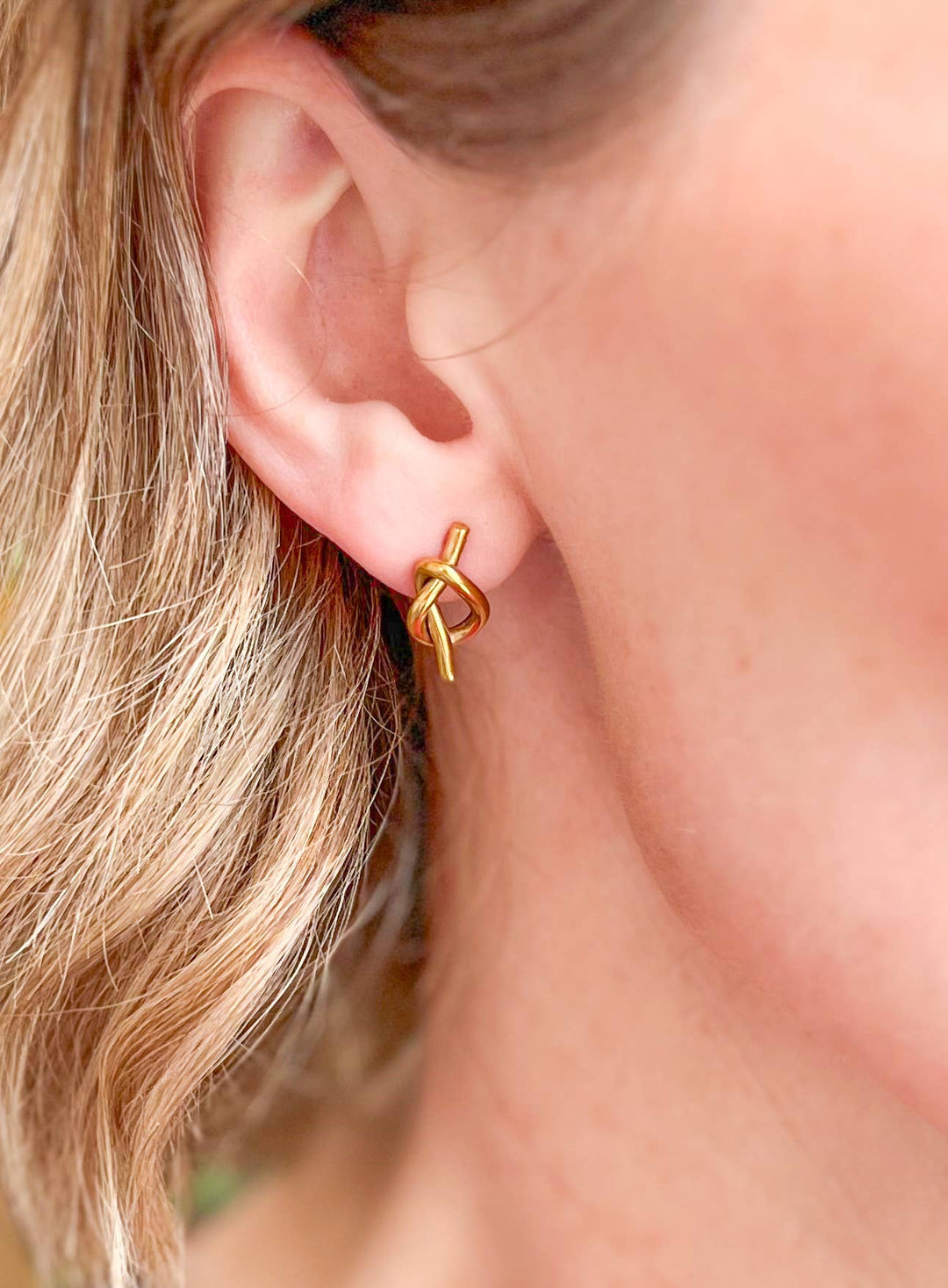 Gold knot stud earring worn by a person with blonde hair.