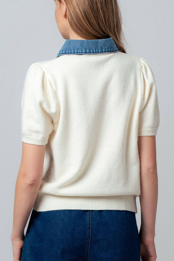 Person wearing a white sweater with a blue denim collar on a plain background