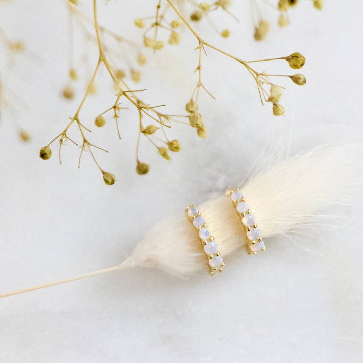 Gold hoop earrings with small opalite stones on a white background with dried flowers.