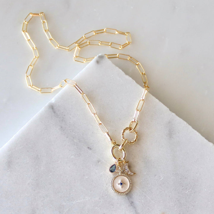 Gold chain necklace with a white and blue pendant on a marble surface