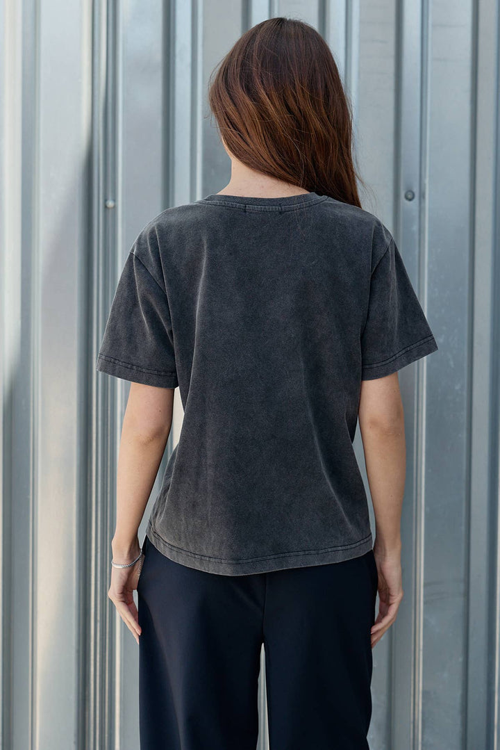 Person wearing a dark gray t-shirt and black pants standing against a corrugated metal wall.