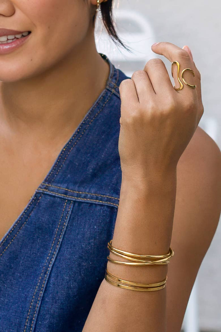 Woman wearing gold jewelry including an adjustable ring, bracelet, and earrings on a blurred background