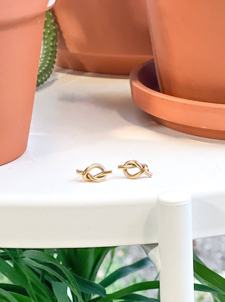 Gold knot earrings on a white surface with terracotta pots in the background
