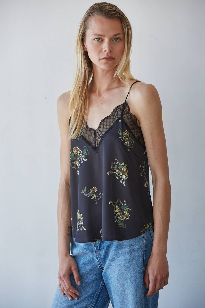 A woman modeling a black camisole top with a lace V-neckline and a leopard print, paired with blue jeans against a plain light gray background.