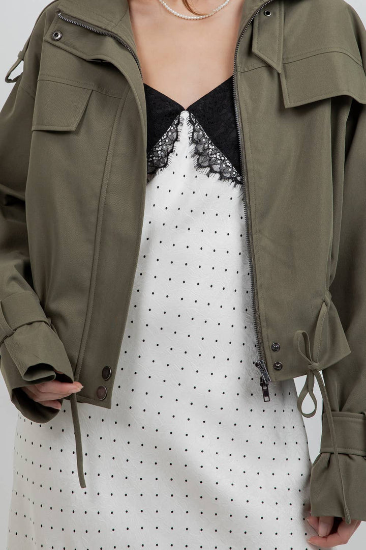 An olive green utility jacket styled over a white and black polka dot dress, shown on a model.