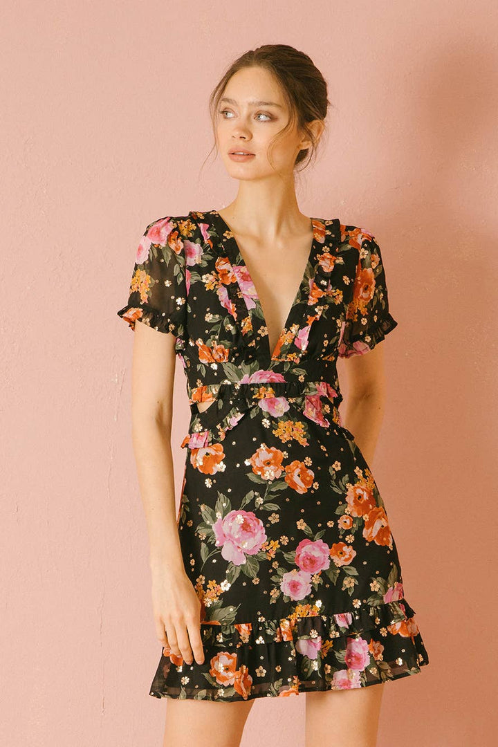 Woman wearing a black floral mini dress against a pink background