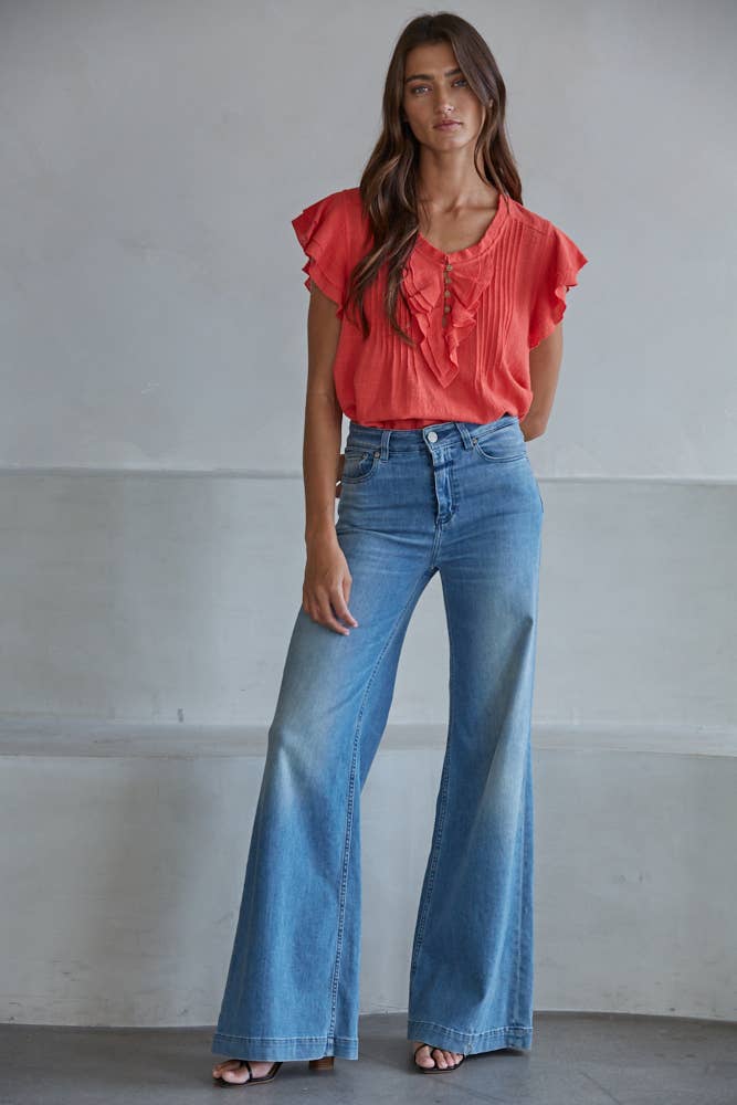 Woman wearing a red blouse and blue jeans against a plain background