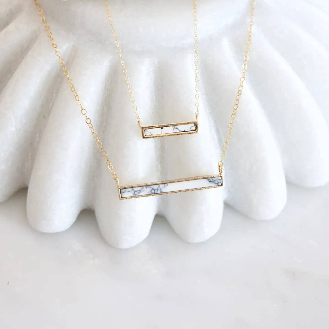 Gold necklace with a bar pendant on a white surface