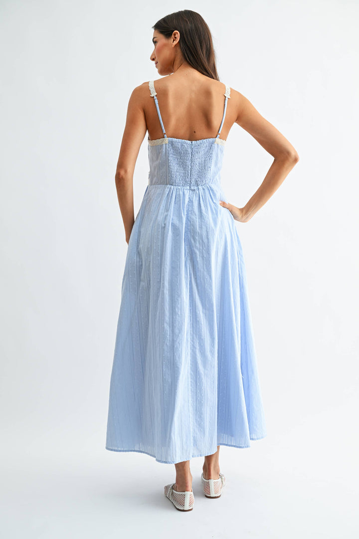Woman wearing a light blue cotton dress with thin straps and lace trim on a white background