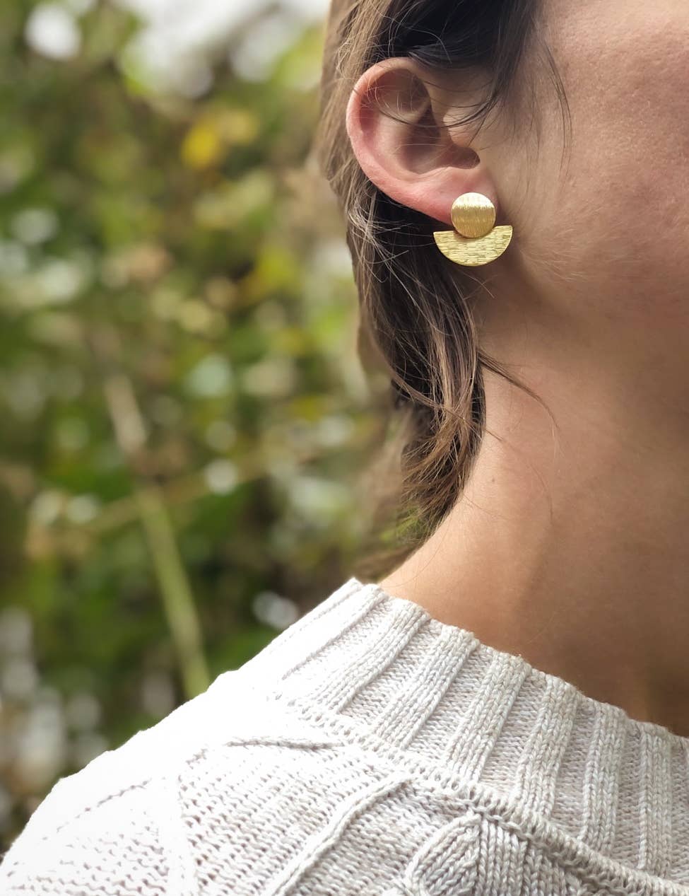 Gold statement earring worn by a woman with a blurred natural background