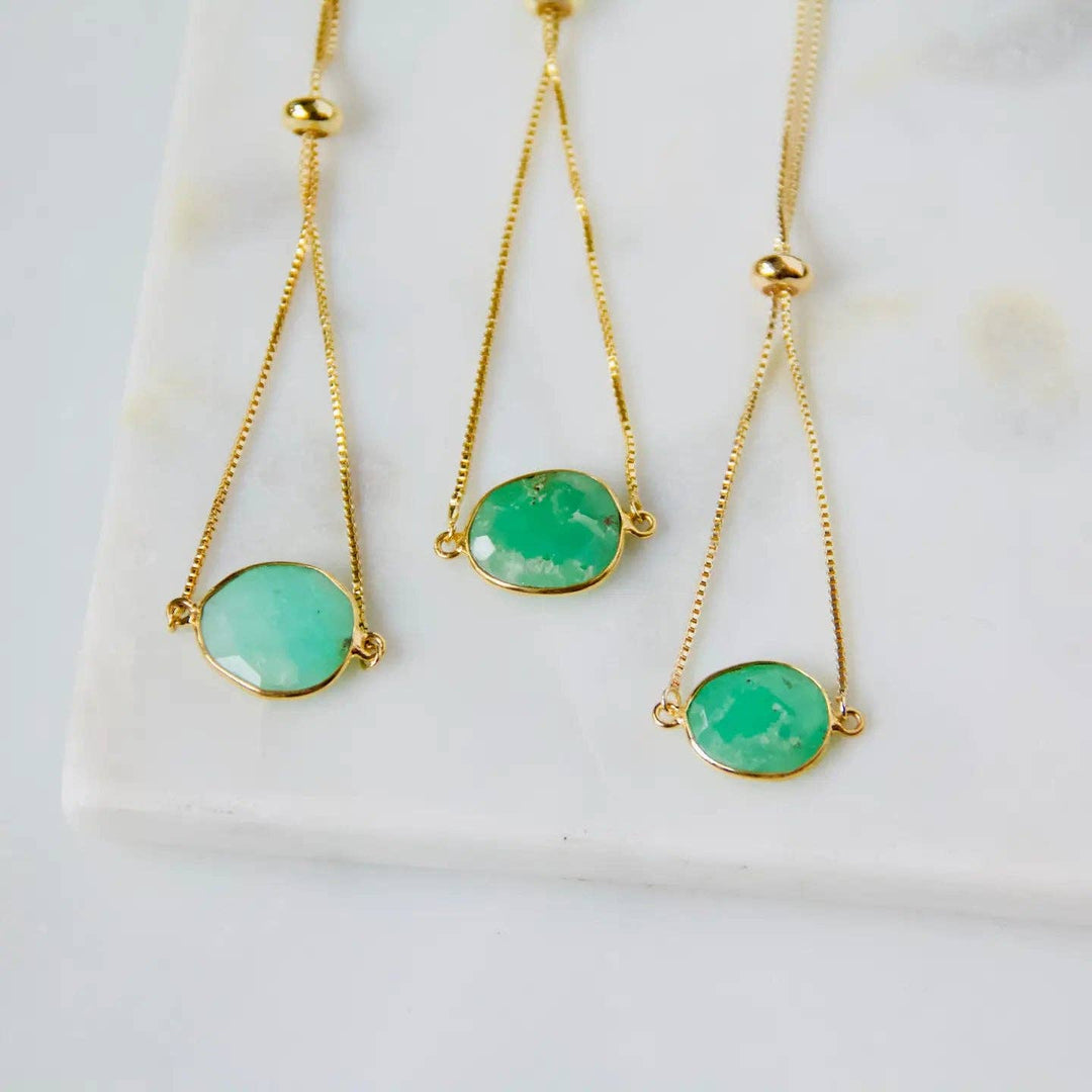 Three gold bracelets with jade green gemstones on a white marble surface