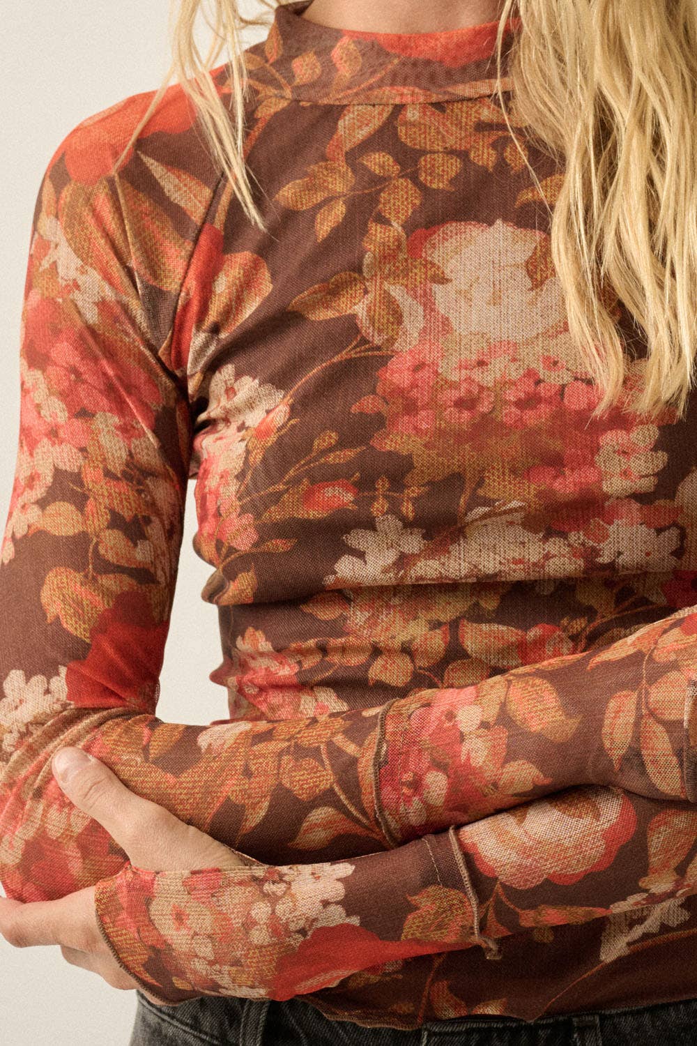 A close-up of a woman wearing a long-sleeve mock neck mesh top with a brown, red, and beige floral pattern.